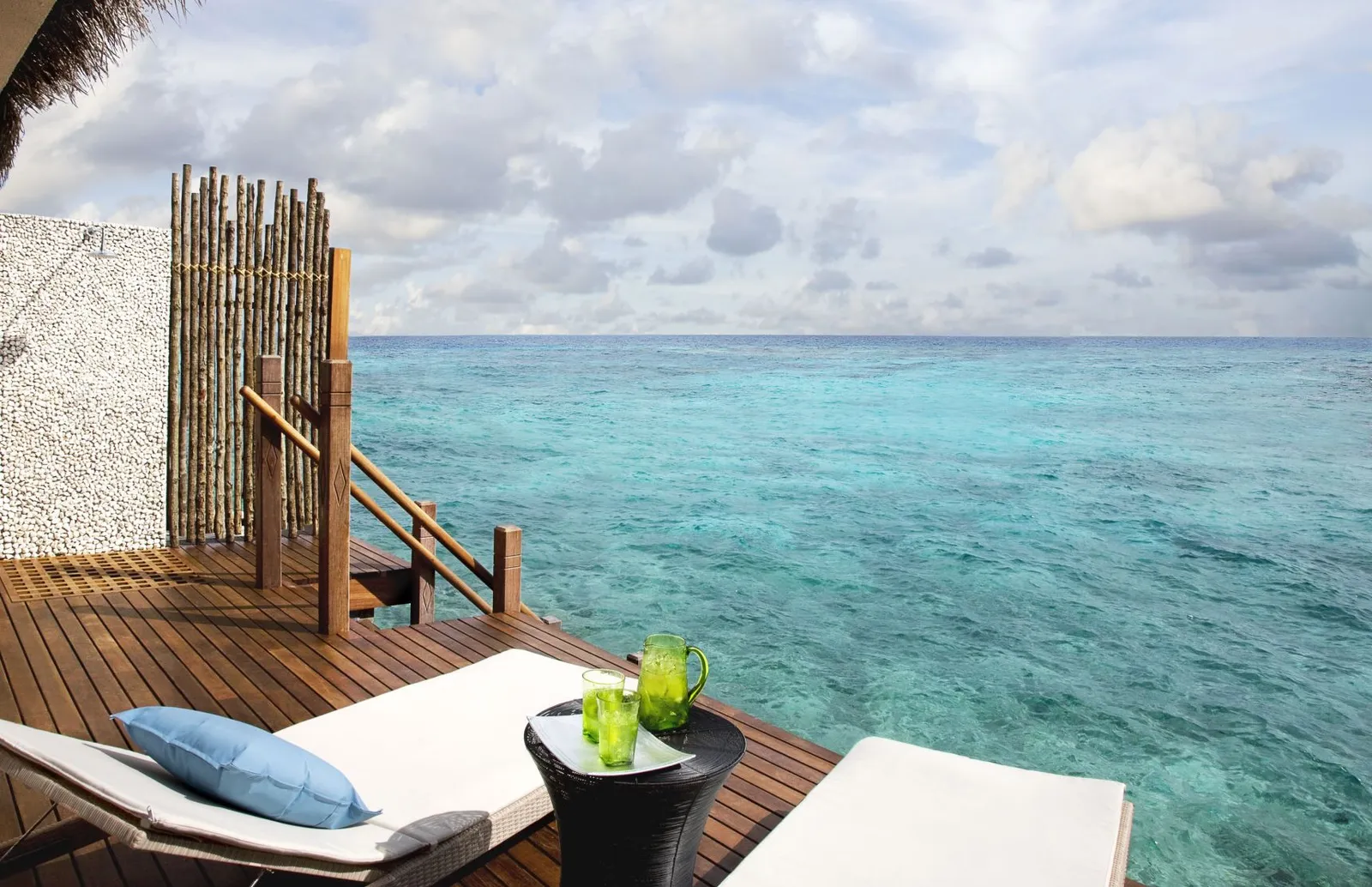 A water villa deck: the lounger, a side table and the ladder down into the lagoon.