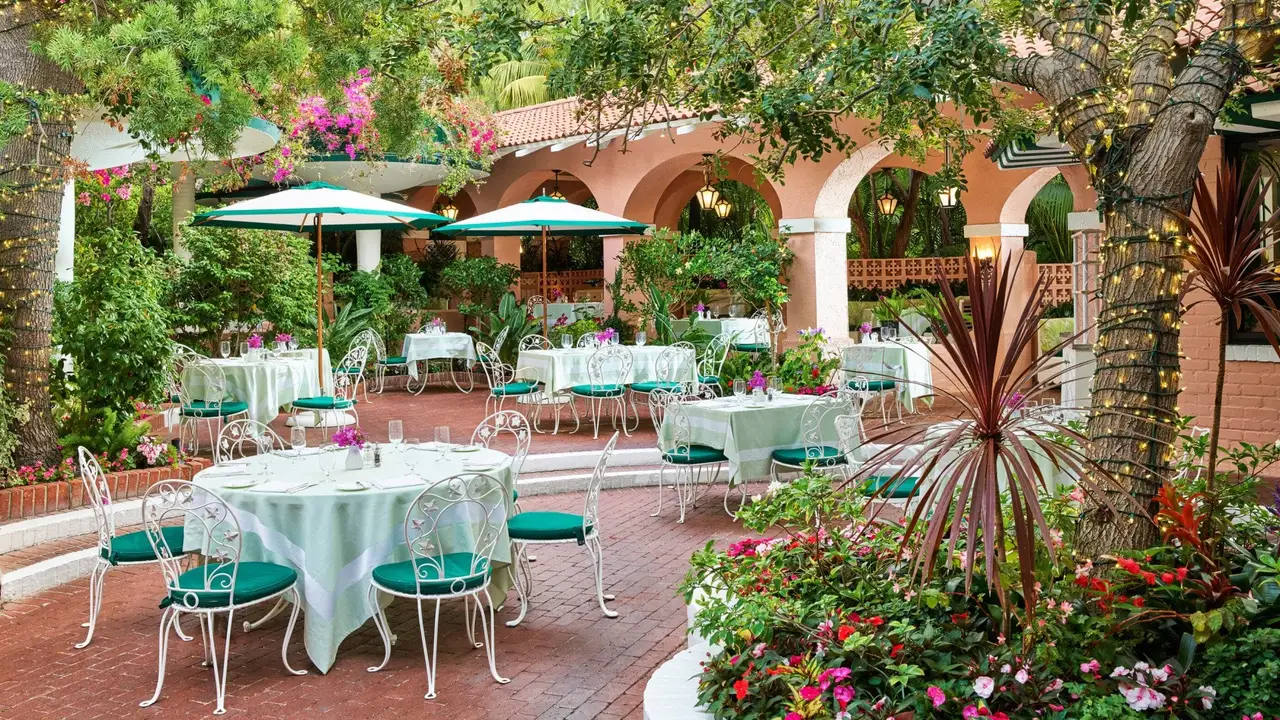 The Polo Lounge patio among bougainvillea and green umbrellas, tables laid in white