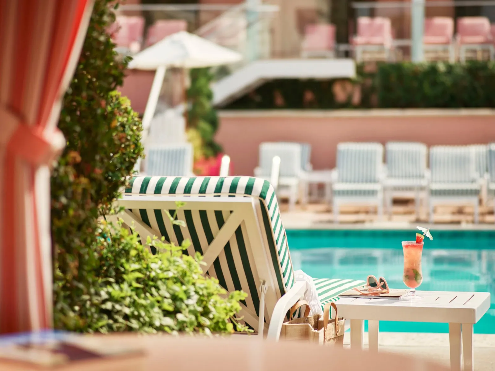 A green-striped lounger by the pool, the pink cabanas behind