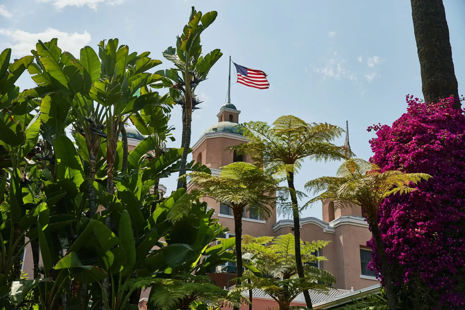 The pink façade with its flag and purple bougainvillea, among palms and ferns
