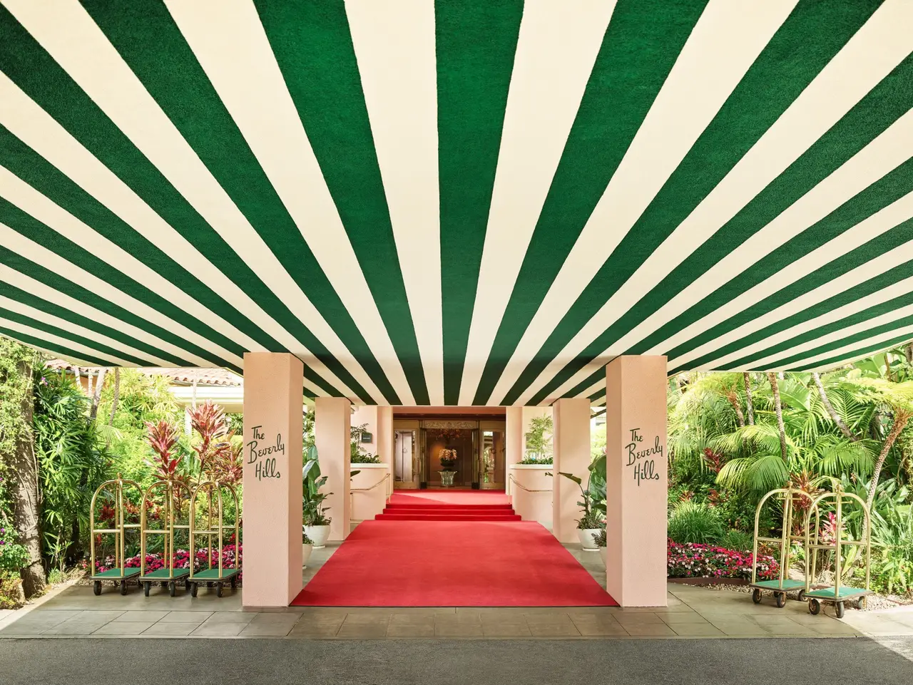 The red carpet under the green-and-white striped awning, between columns bearing the hotel’s name