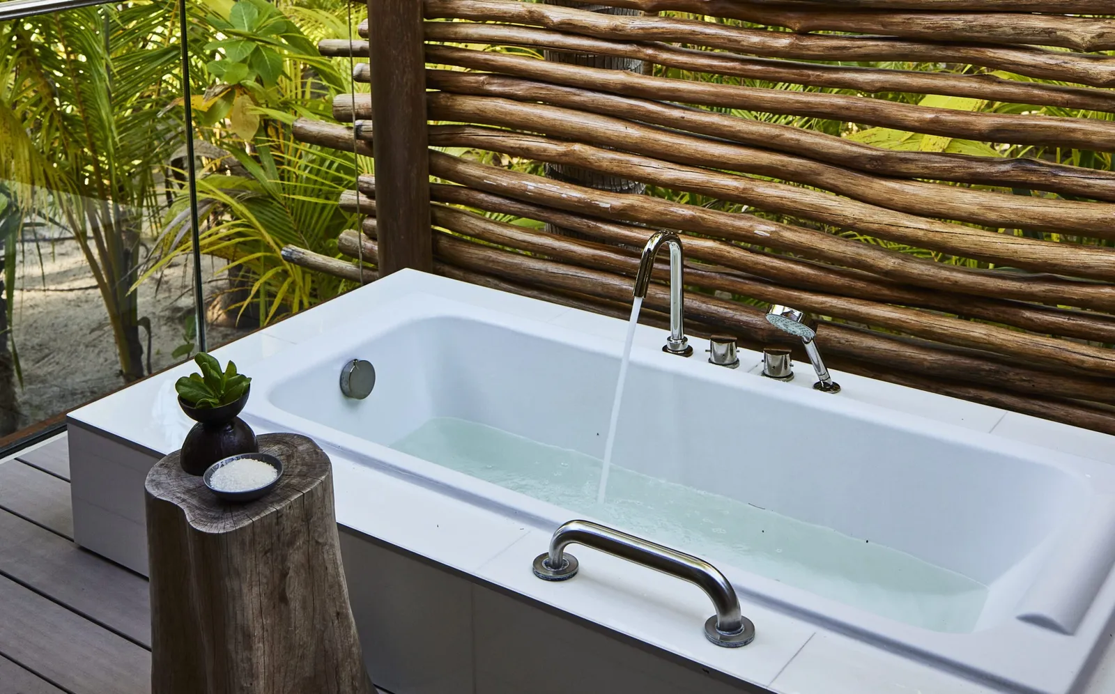 A villa’s outdoor bathtub on a deck screened by branches