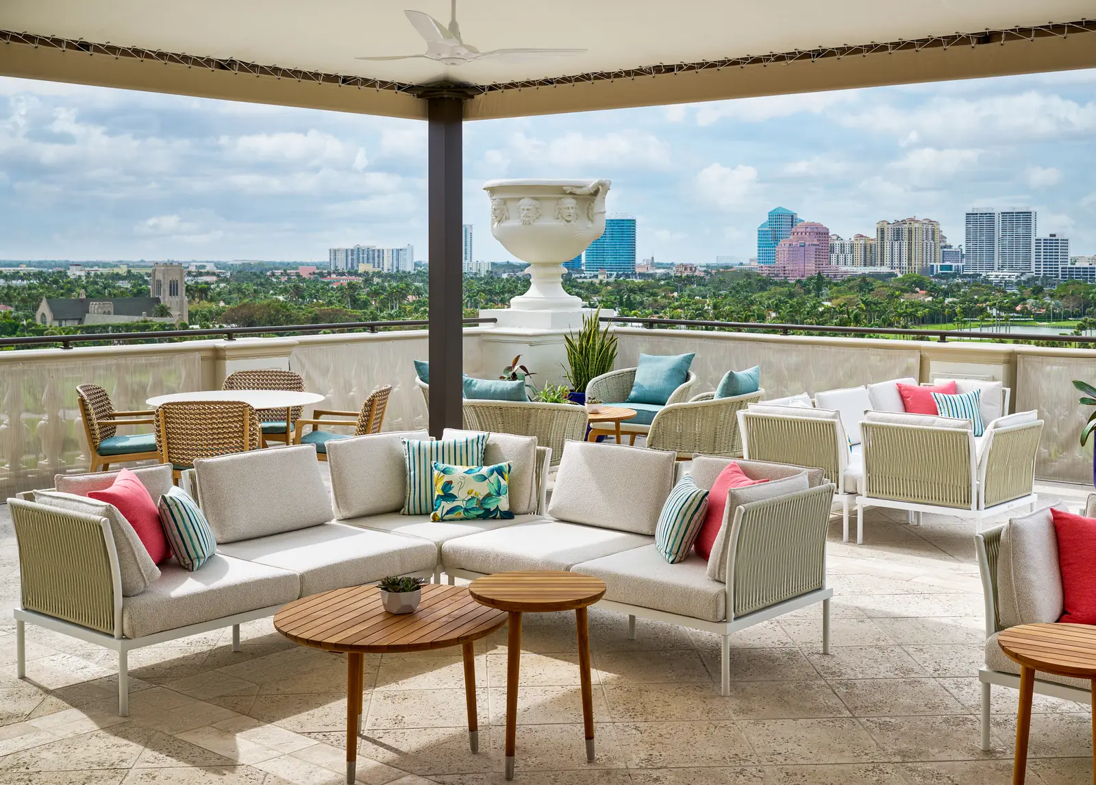 The Flagler Club terrace: pale sofas and wooden tables under the canopy, looking over the golf course to the towers of West Palm Beach.