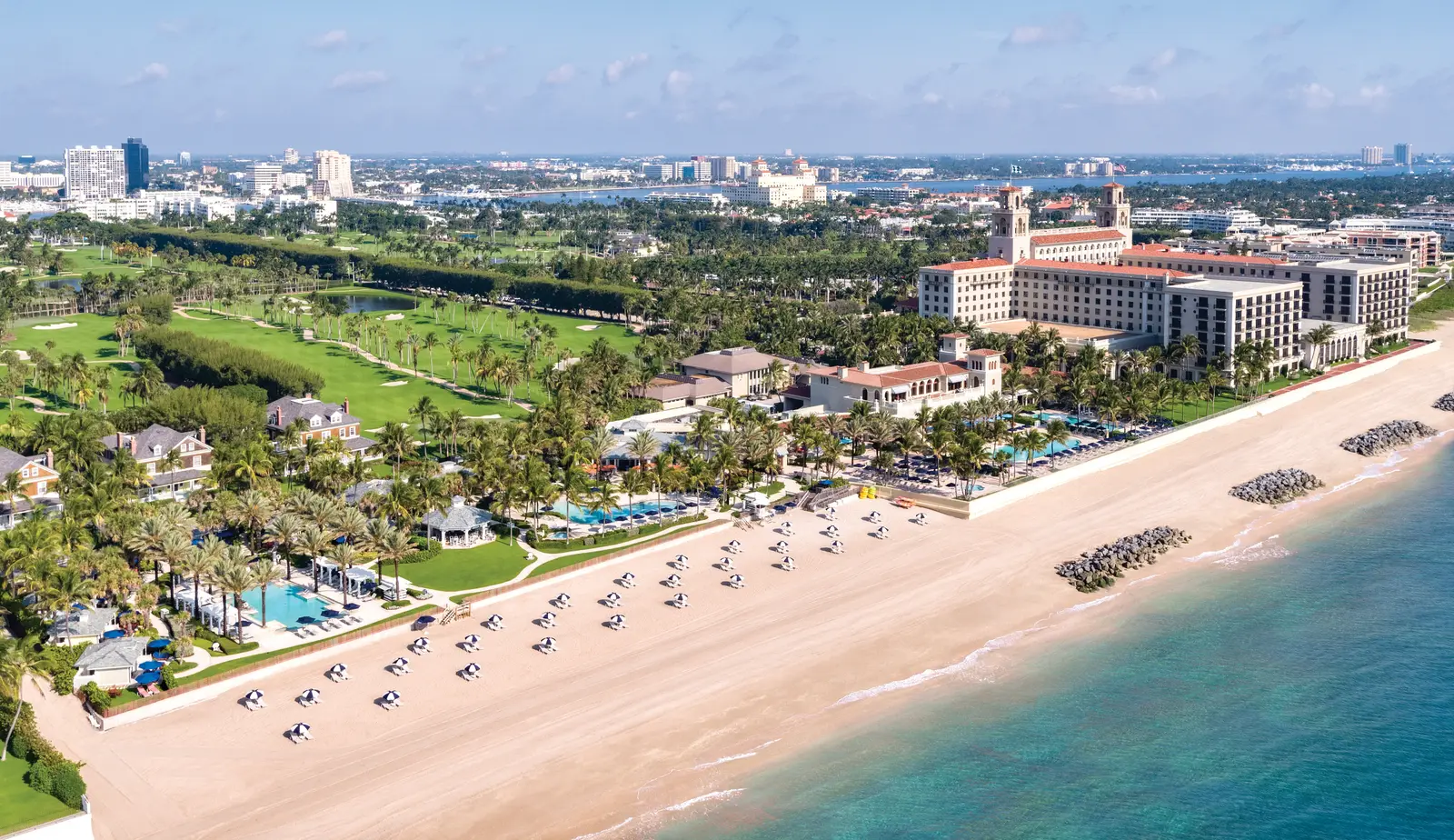 The beach from the air: sand dotted with blue parasols, the pools among the palms, the golf course and the twin-towered hotel behind.