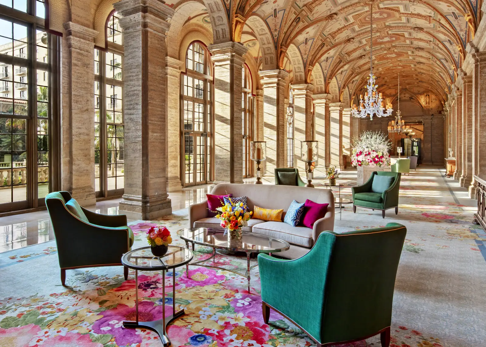 The lobby: a gallery of stone arches under a painted vault, arched windows, a crystal chandelier and green armchairs on a floral carpet.