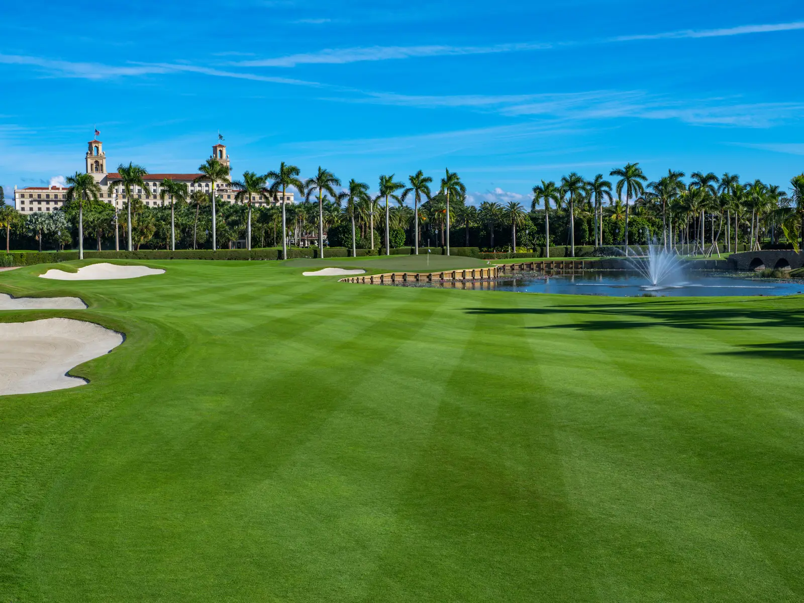 The Ocean Course: a striped fairway, a bunker, a pond with a fountain and the hotel’s towers beyond the palms.