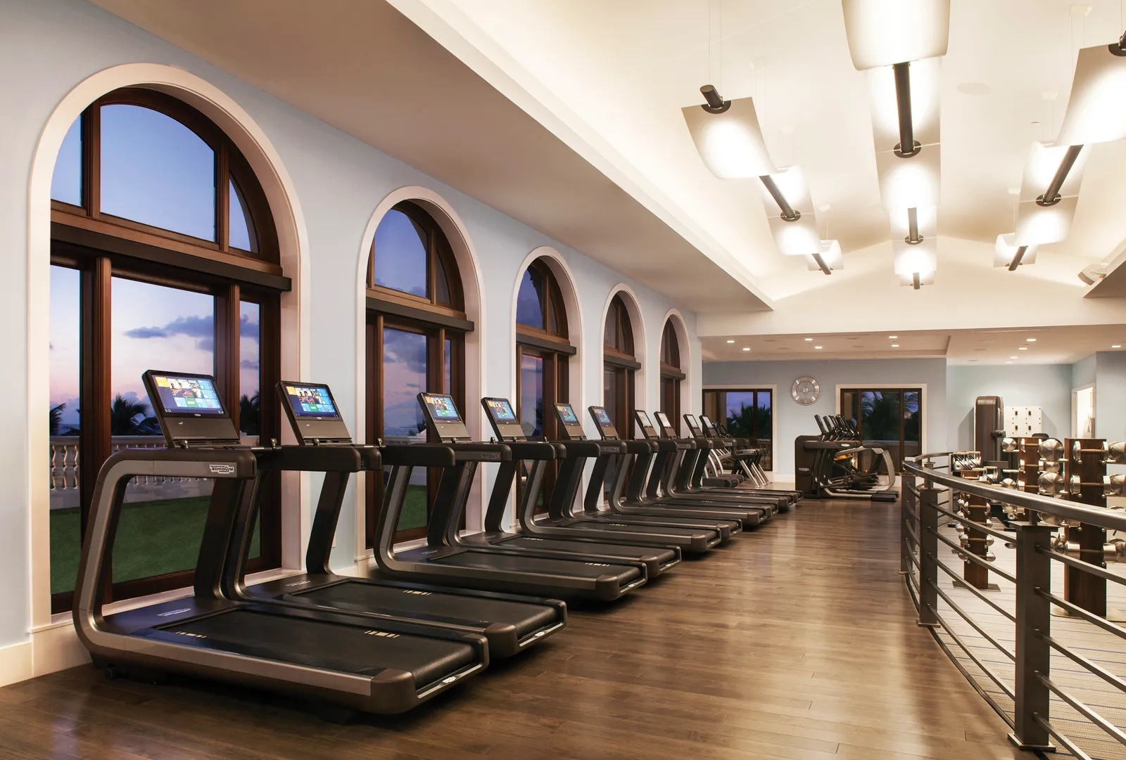 Ocean Fitness: a row of treadmills facing the arched windows, on a timber floor with the ocean outside.