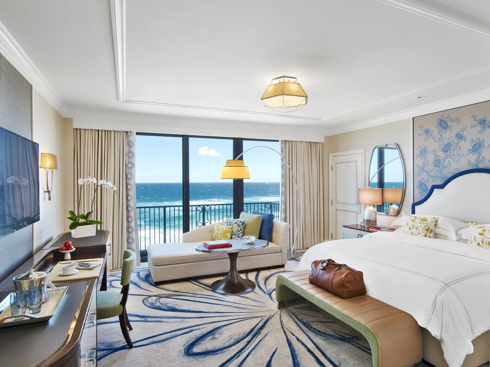 An Atlantic Guest Room: the bed with a bench at its foot, a chaise longue and the glass door open to a Juliet balcony with the ocean in front.