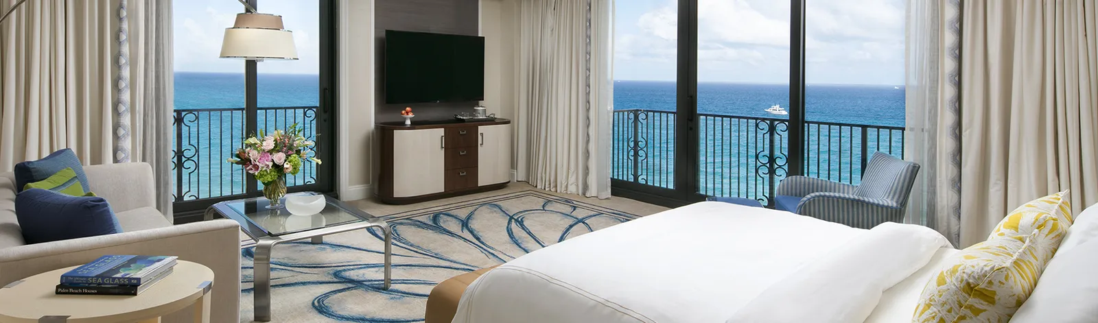 An Atlantic Junior Suite: the bed in front, the television between 2 glass doors onto the ocean and an armchair on either side.