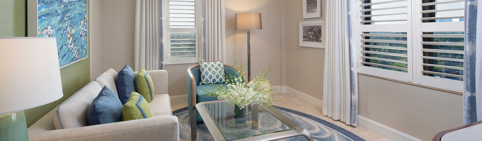 A Classic Suite’s sitting room: the sofa with blue and green cushions, a glass table and white shutters at the windows.