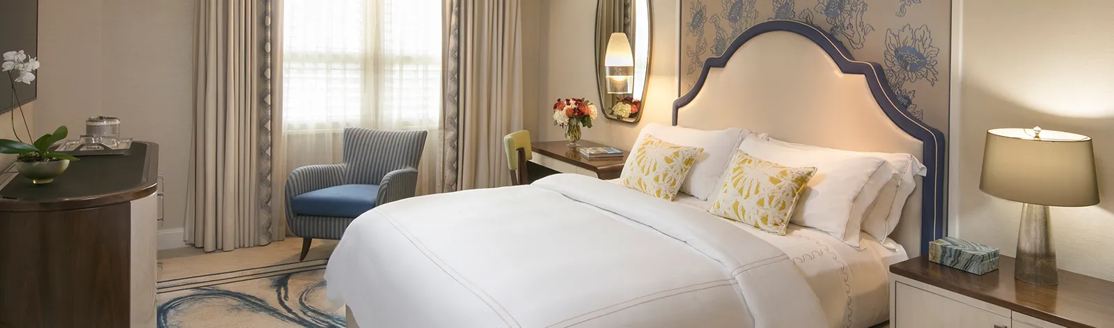 A Deluxe Guest Room with resort view: the king bed with yellow cushions, a blue armchair and the window behind pale curtains.