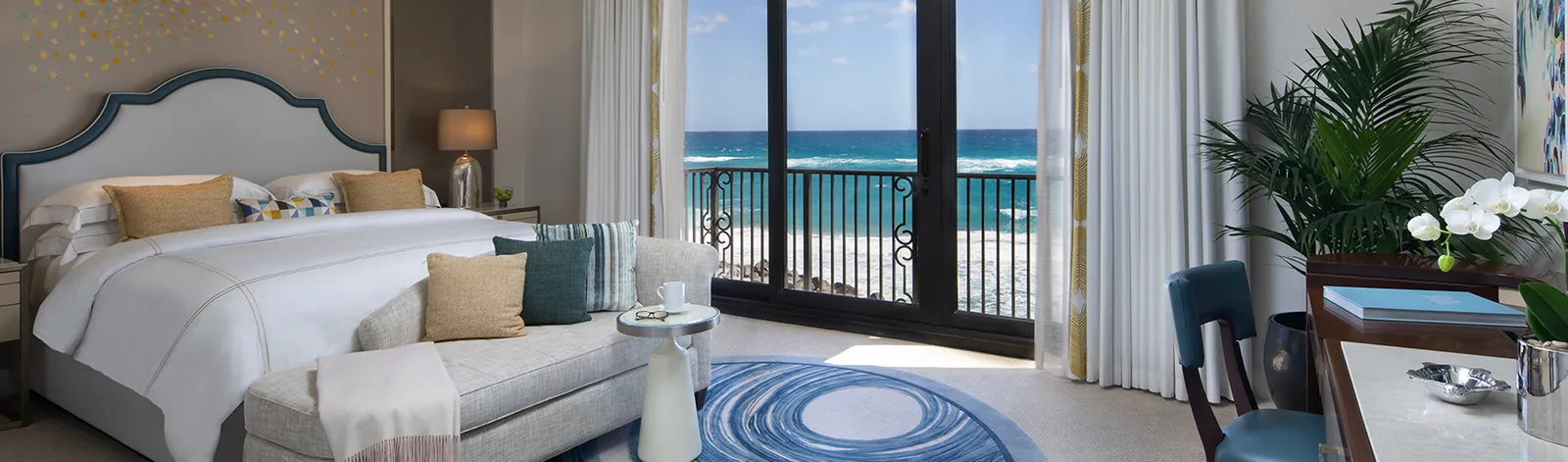 The Executive Suite’s bedroom: the bed with its shaped headboard, a chaise at its foot and the glass door with the waves just beyond the Juliet balcony.