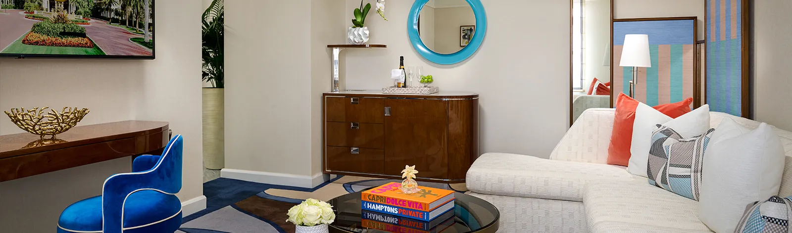 A Flagler Club Classic Suite’s sitting room: a white sofa, an electric-blue armchair, a wooden bar cabinet and a round turquoise mirror.