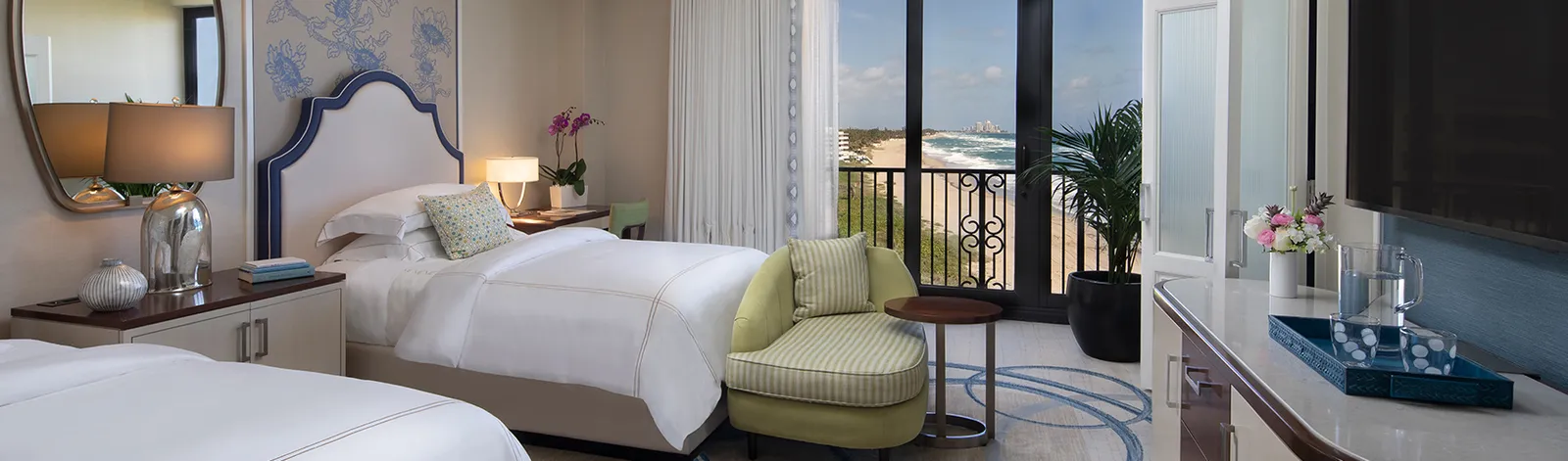 A Premium Guest Room with 2 beds, a green armchair and a railed glass door with a view of the coast.