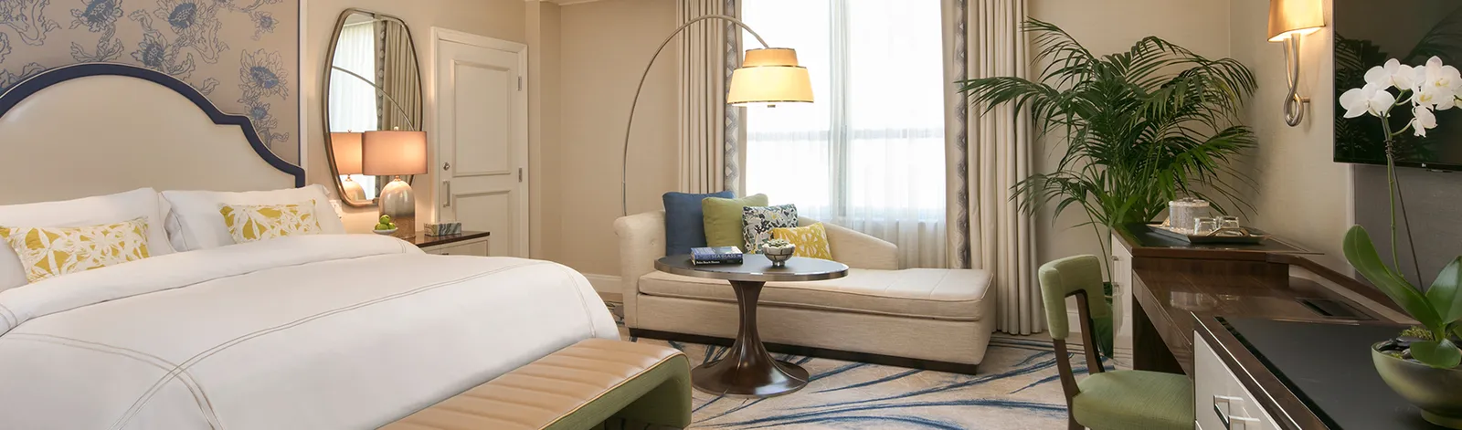 A Premium Guest Room with resort view: the king bed with its shaped headboard, a small sofa and a potted palm by the window.