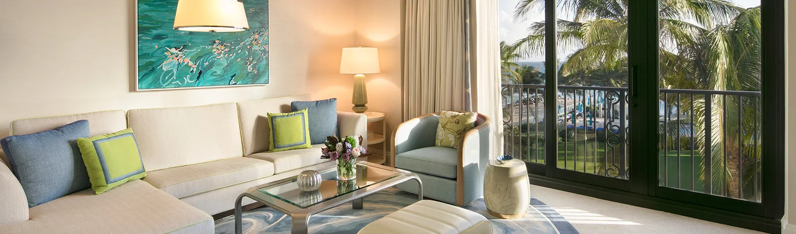 A Premium Suite’s sitting room: the pale sofa, 2 lamps and the railed glass door open onto the palms.