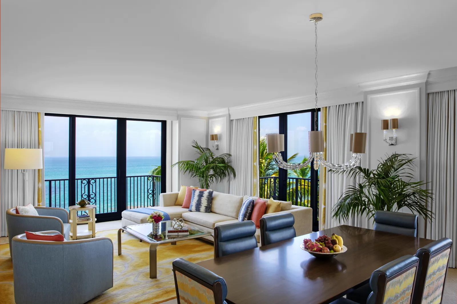 The Royal Poinciana Suite’s living room: the dark wood dining table, the sofas and the railed glass doors onto the sea.