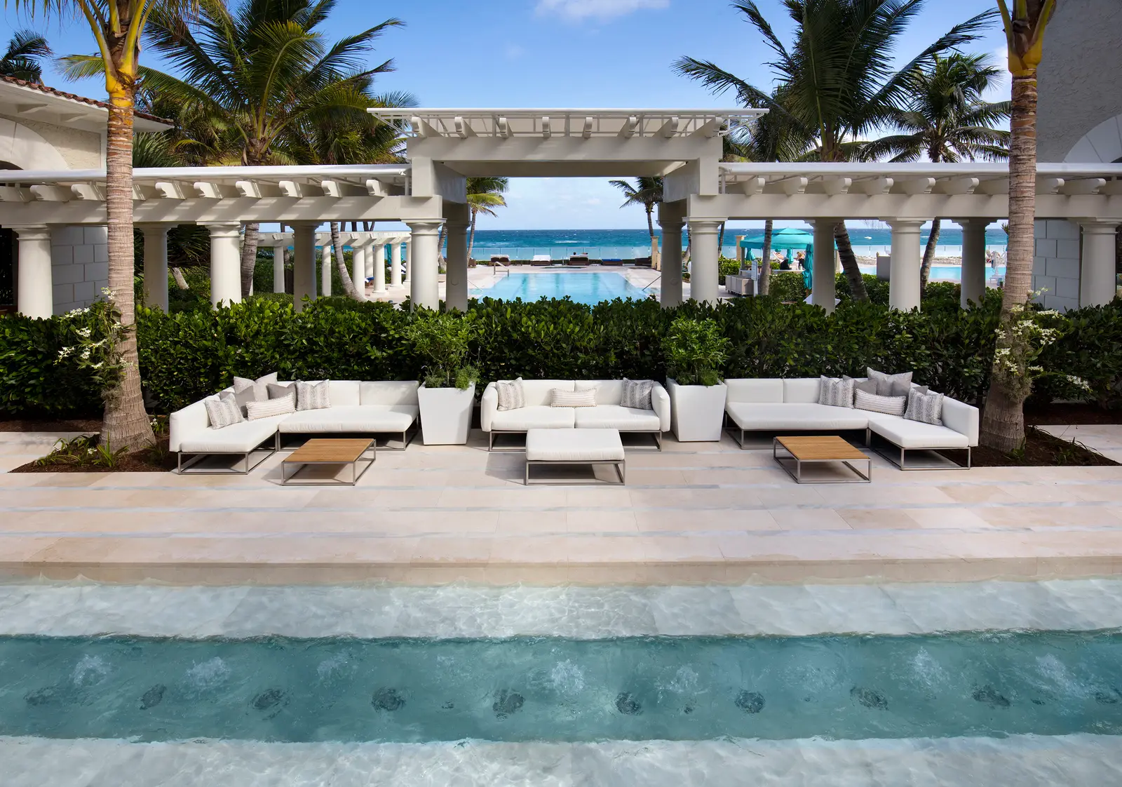 The spa courtyard: white sofas under a pergola, a pool of water in front, palms and the ocean beyond.