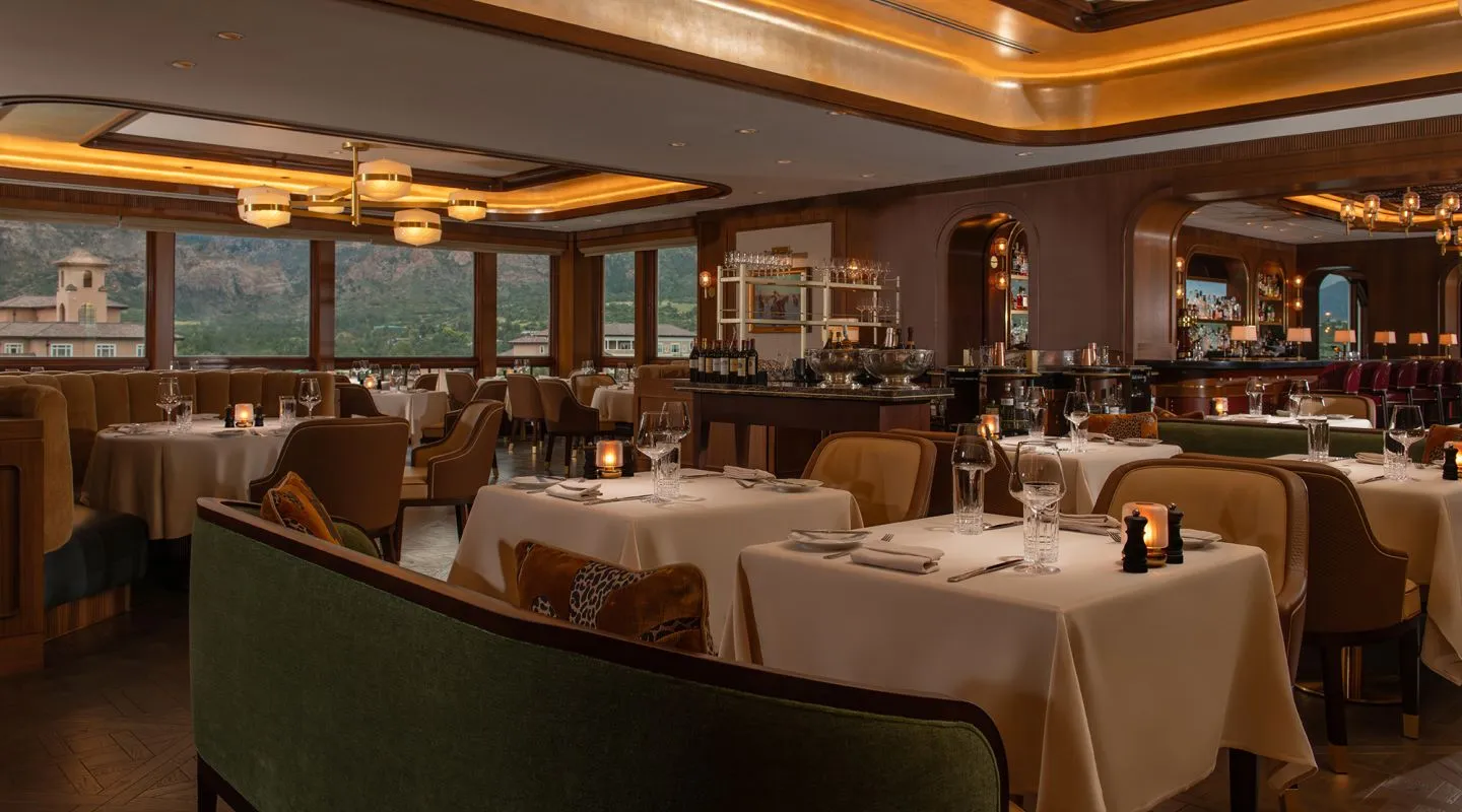 A Broadmoor dining room with tall windows, laid tables and green sofas