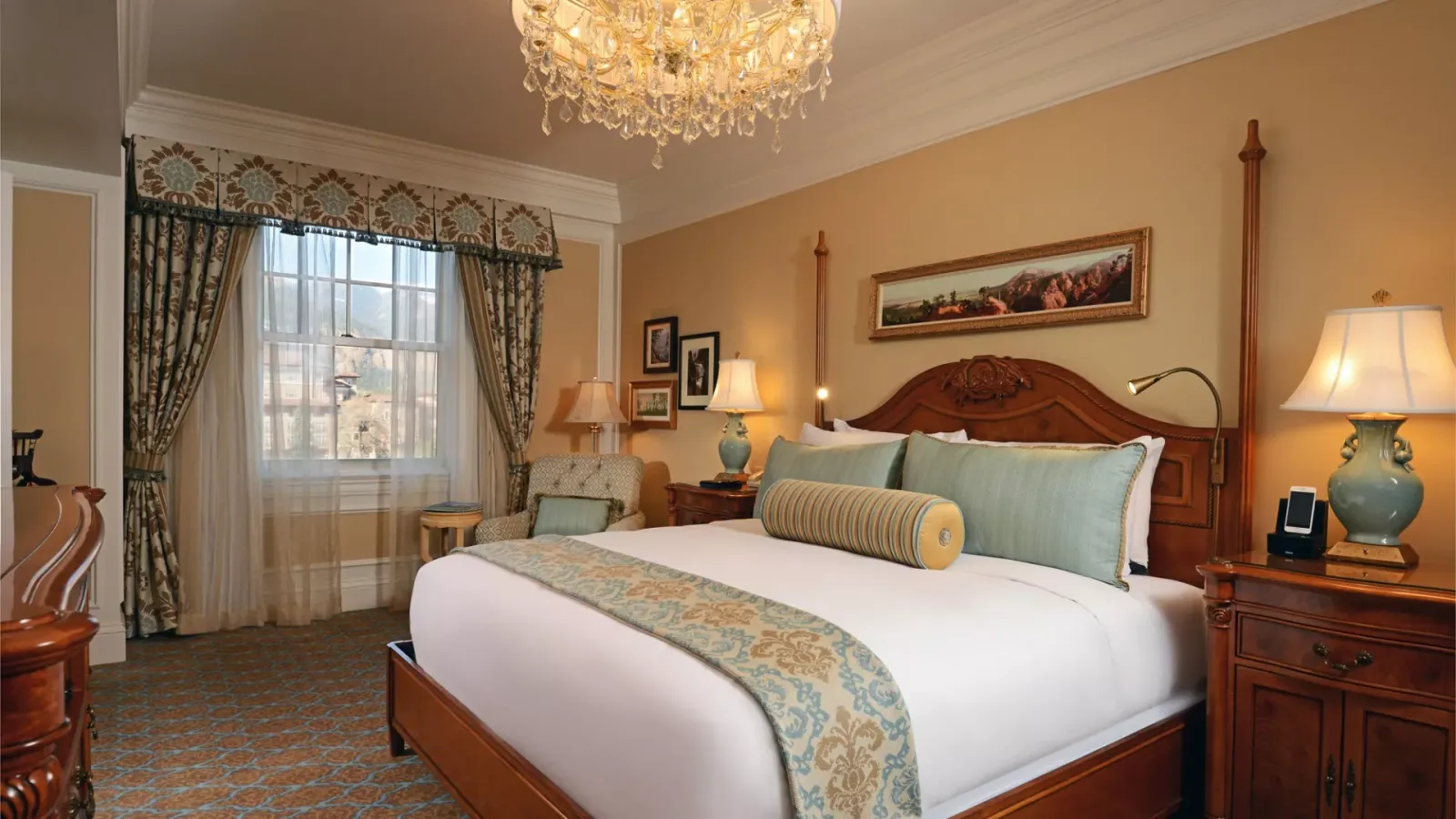 A Broadmoor bedroom: upholstered headboard, swagged curtains, a chandelier and an armchair