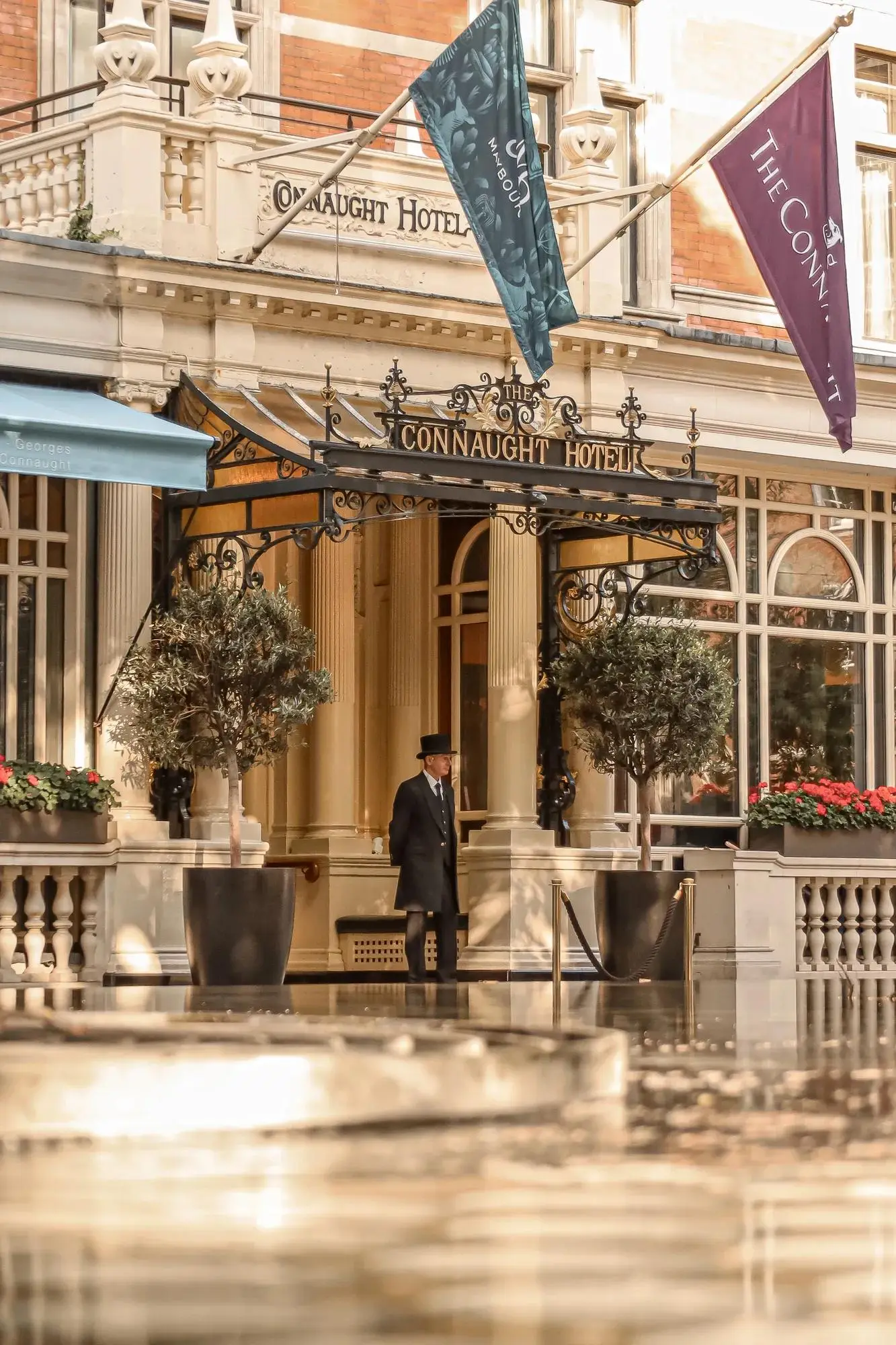 The Connaught’s entrance on Carlos Place: a doorman in a top hat, lamps, potted trees and the hotel’s flags