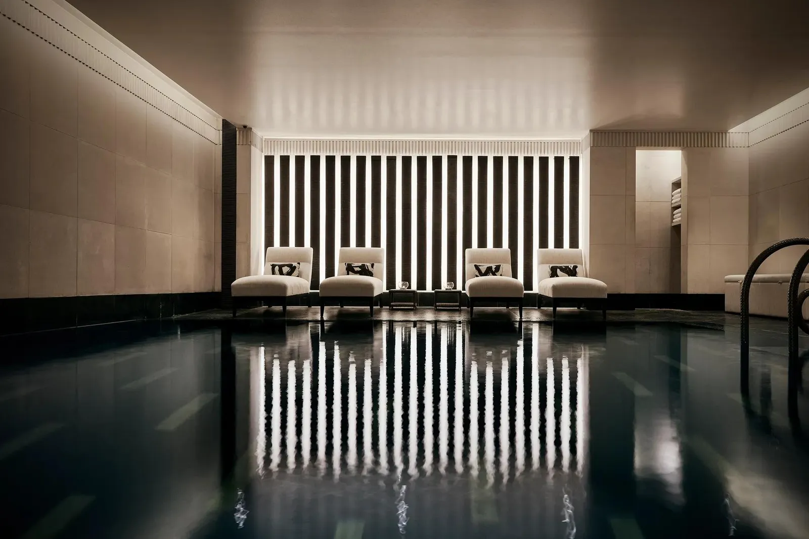 The Aman Spa pool: dark water reflecting a wall of black and white stripes and 4 loungers