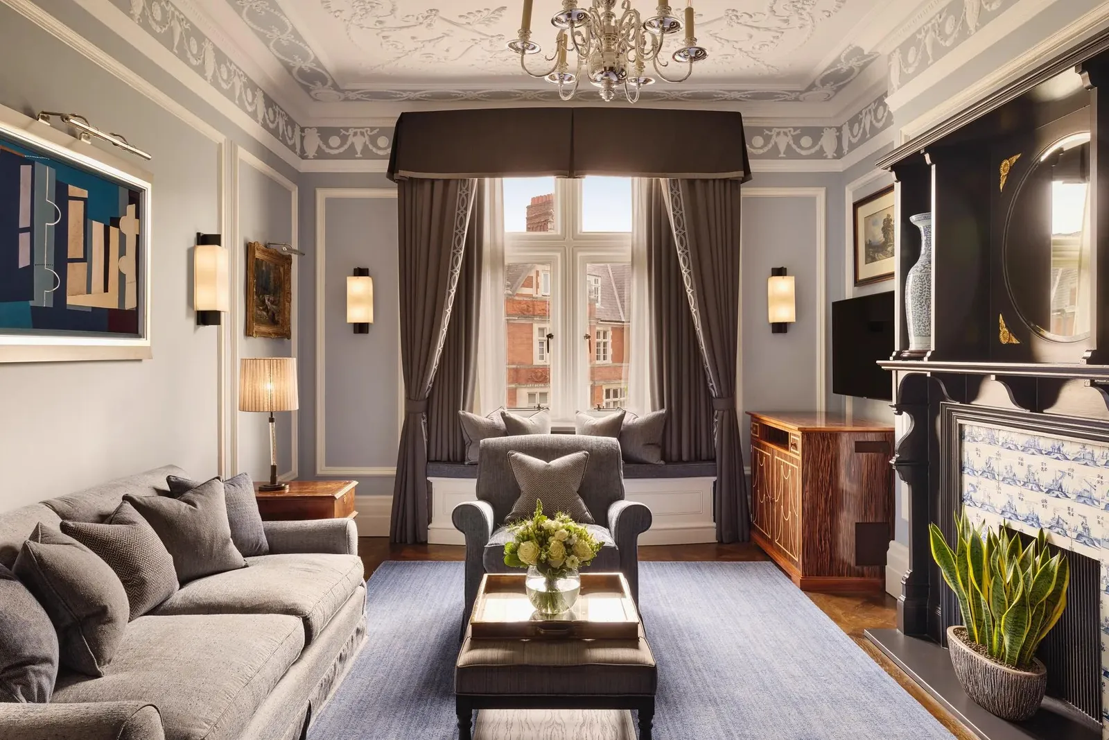 The Carlos Suite: a plasterwork ceiling, a chandelier, a blue-tiled fireplace and a grey sofa