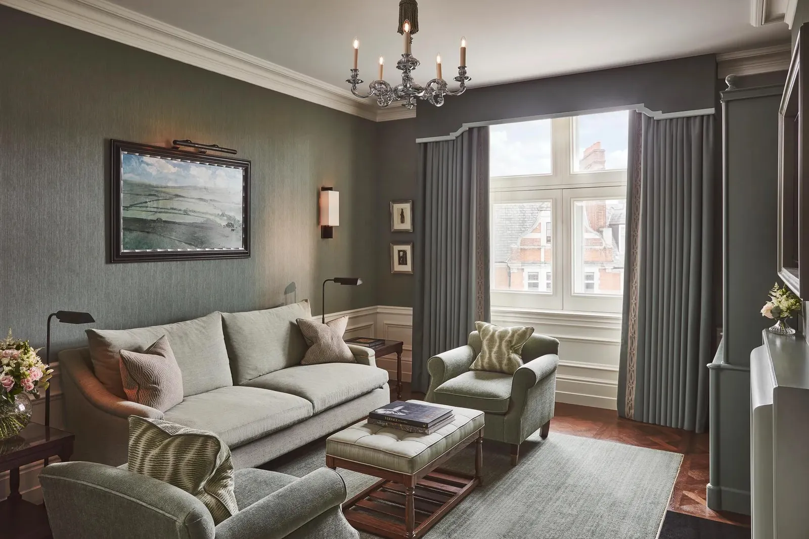 The Coburg Suite: a sage-green sitting room with a chandelier, a pale sofa and a seascape on the wall