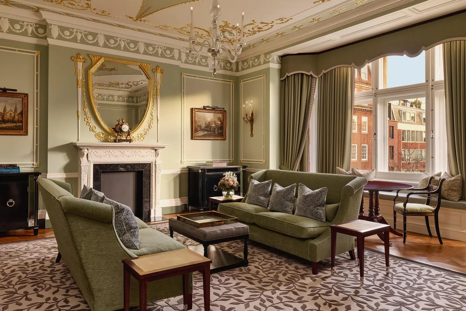The Connaught Suite: a gilt mirror over a marble fireplace, green sofas and windows onto Mayfair brick