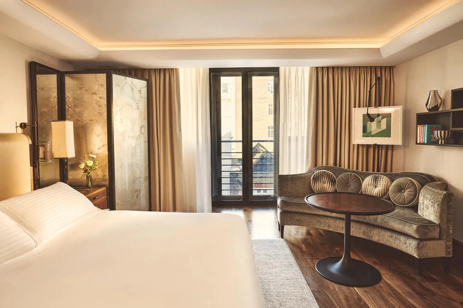 A Contemporary Deluxe Room: dark parquet, a white bed, a velvet sofa and French windows with a small balcony