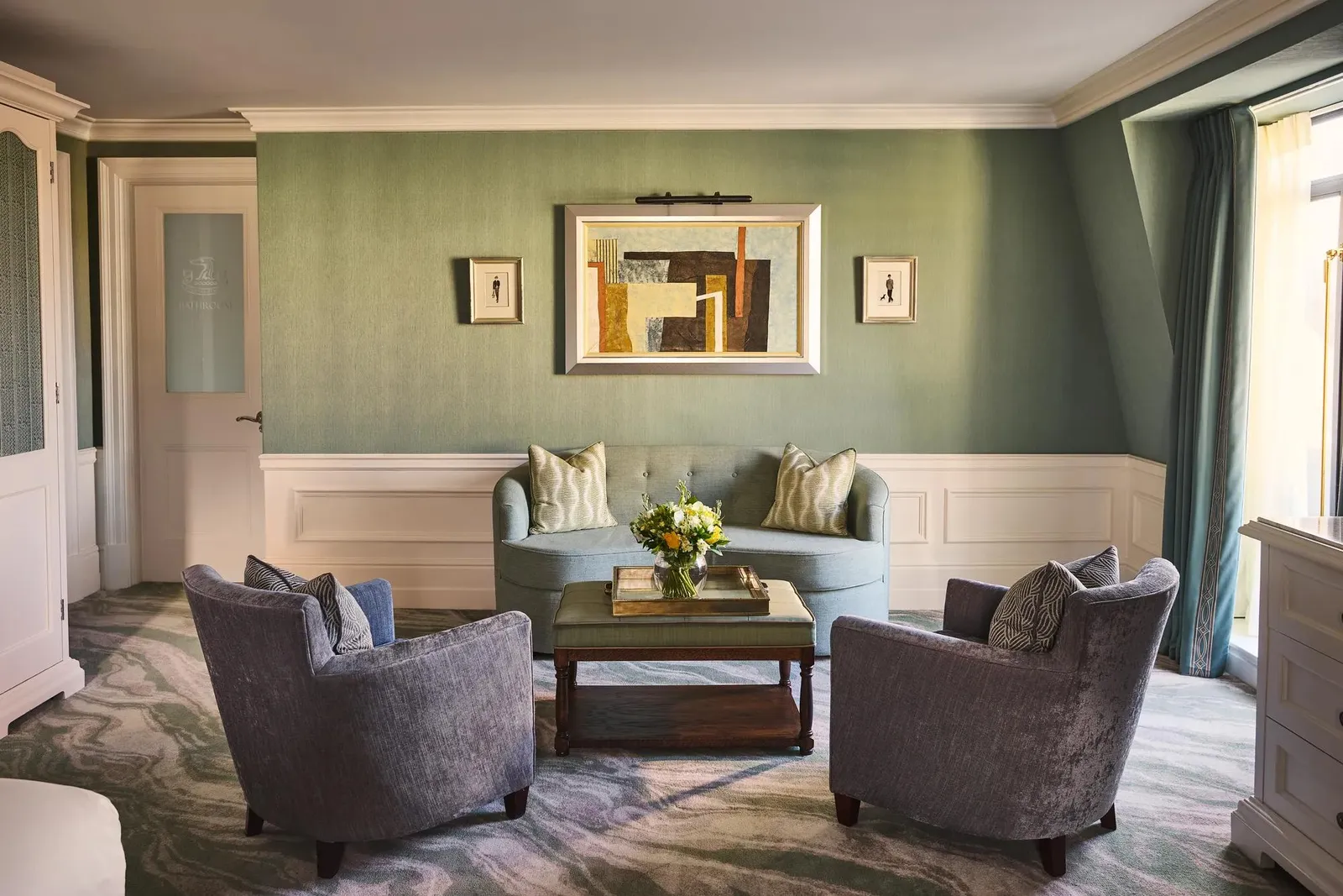 A Deluxe Junior Suite: a sitting room with blue armchairs, white panelling and an abstract painting in a gilt frame