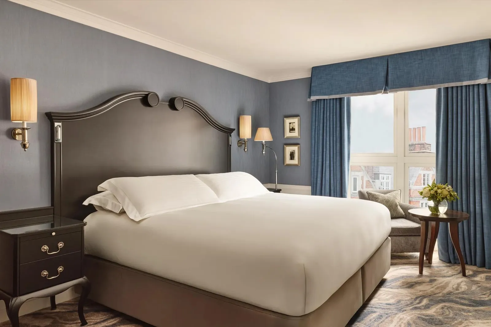 A Deluxe Room: a king bed, blue walls and an armchair by a window over the rooftops