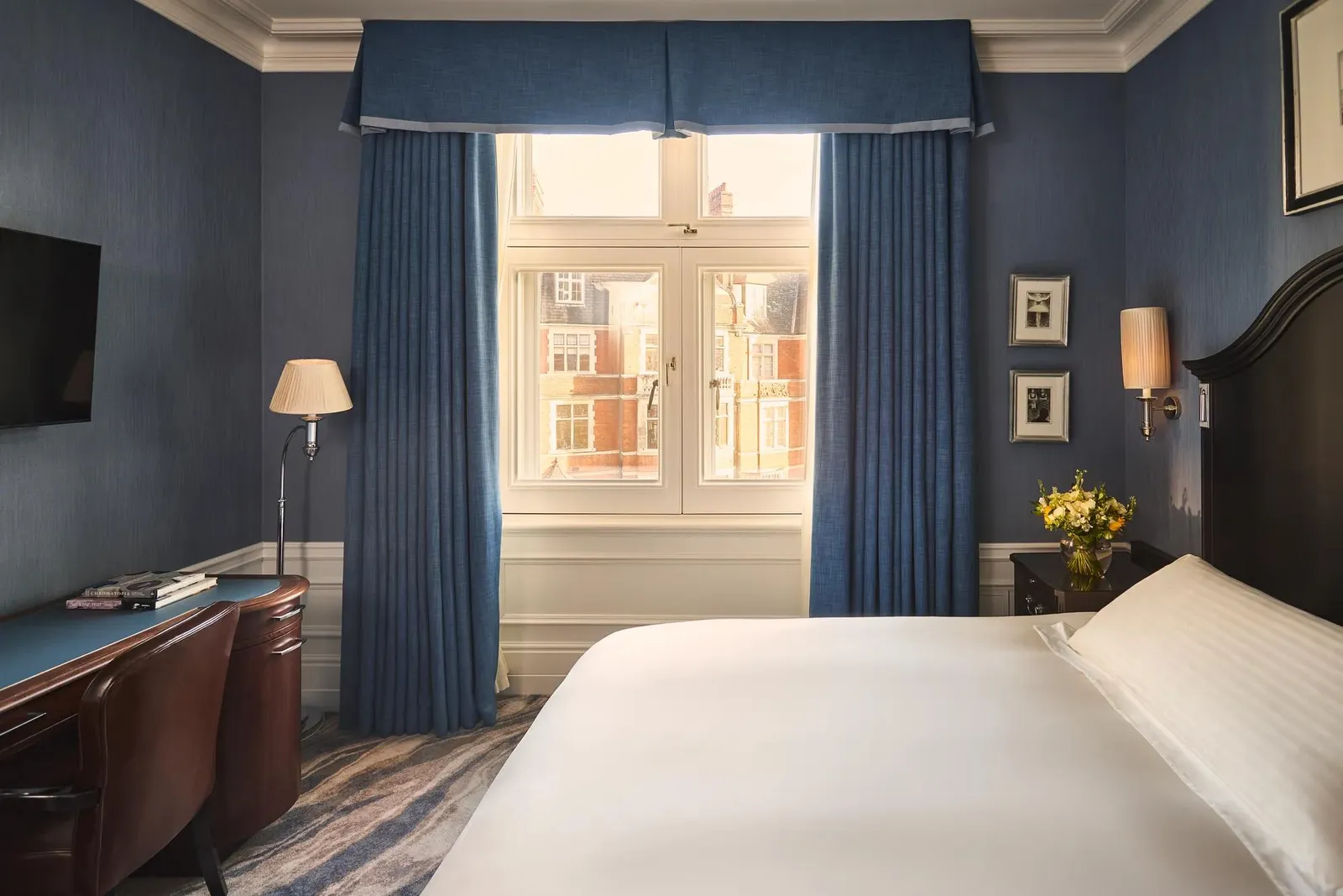 A Superior Single: a bed with a dark headboard, blue walls and a desk under the window over brick rooftops