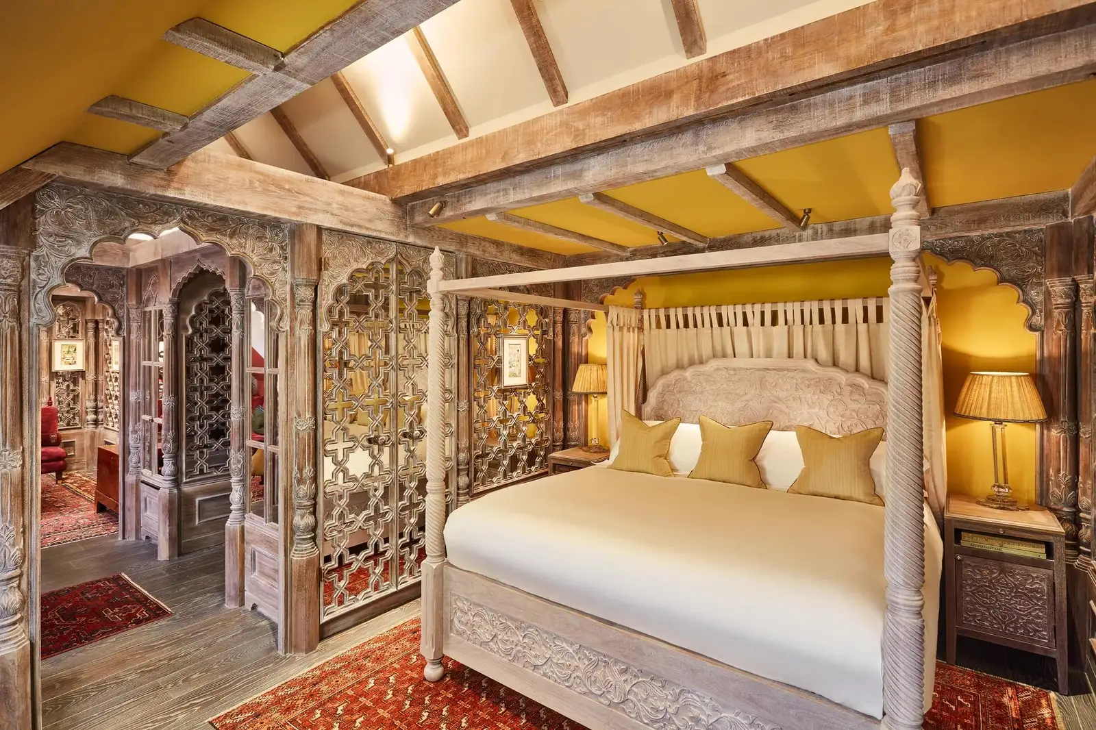 One of the Lodges: a white four-poster, exposed beams painted yellow and carved wooden screens