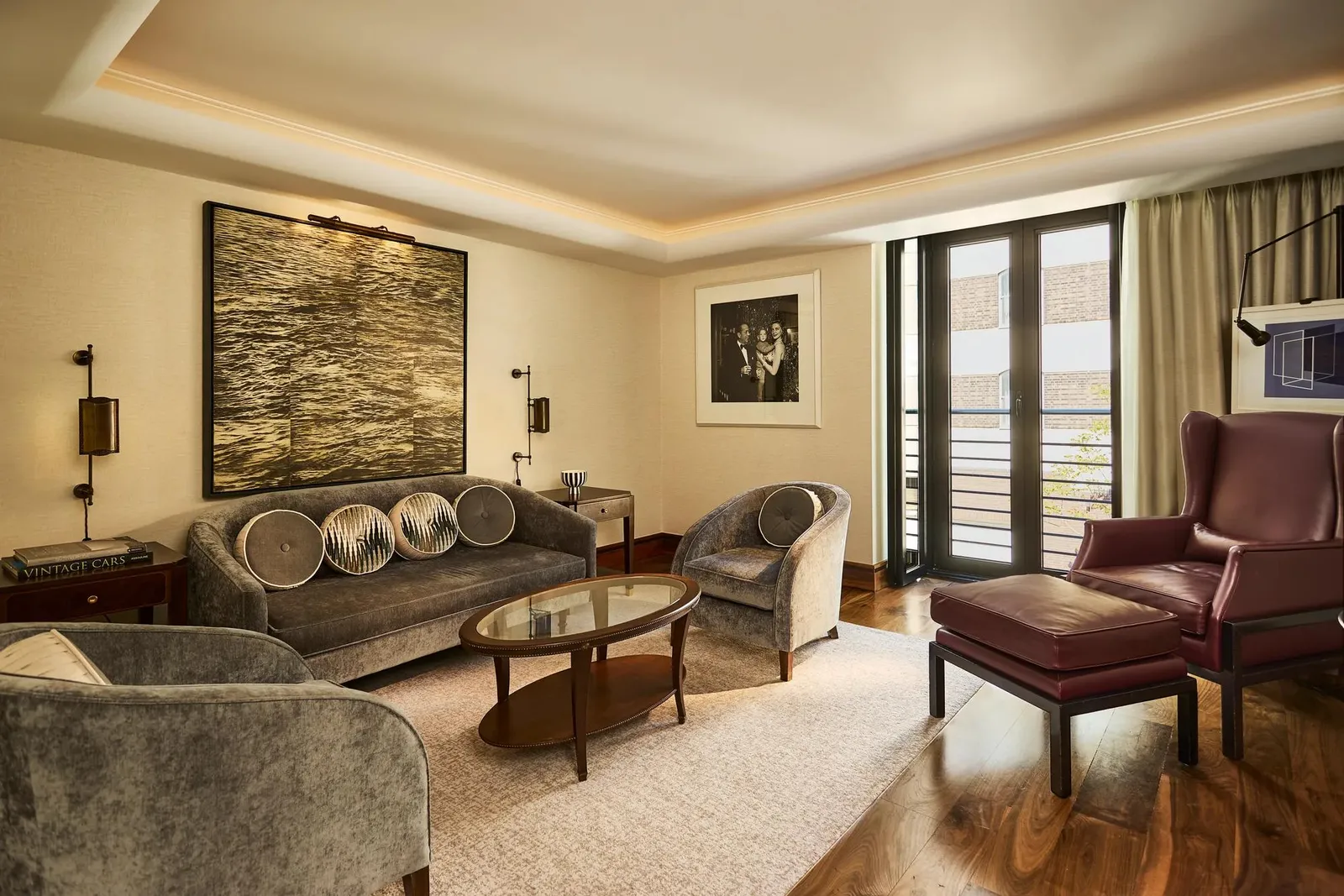 The Two Bedroom Adams Suite: a sitting room with a velvet sofa, an oxblood leather armchair and a large dark canvas