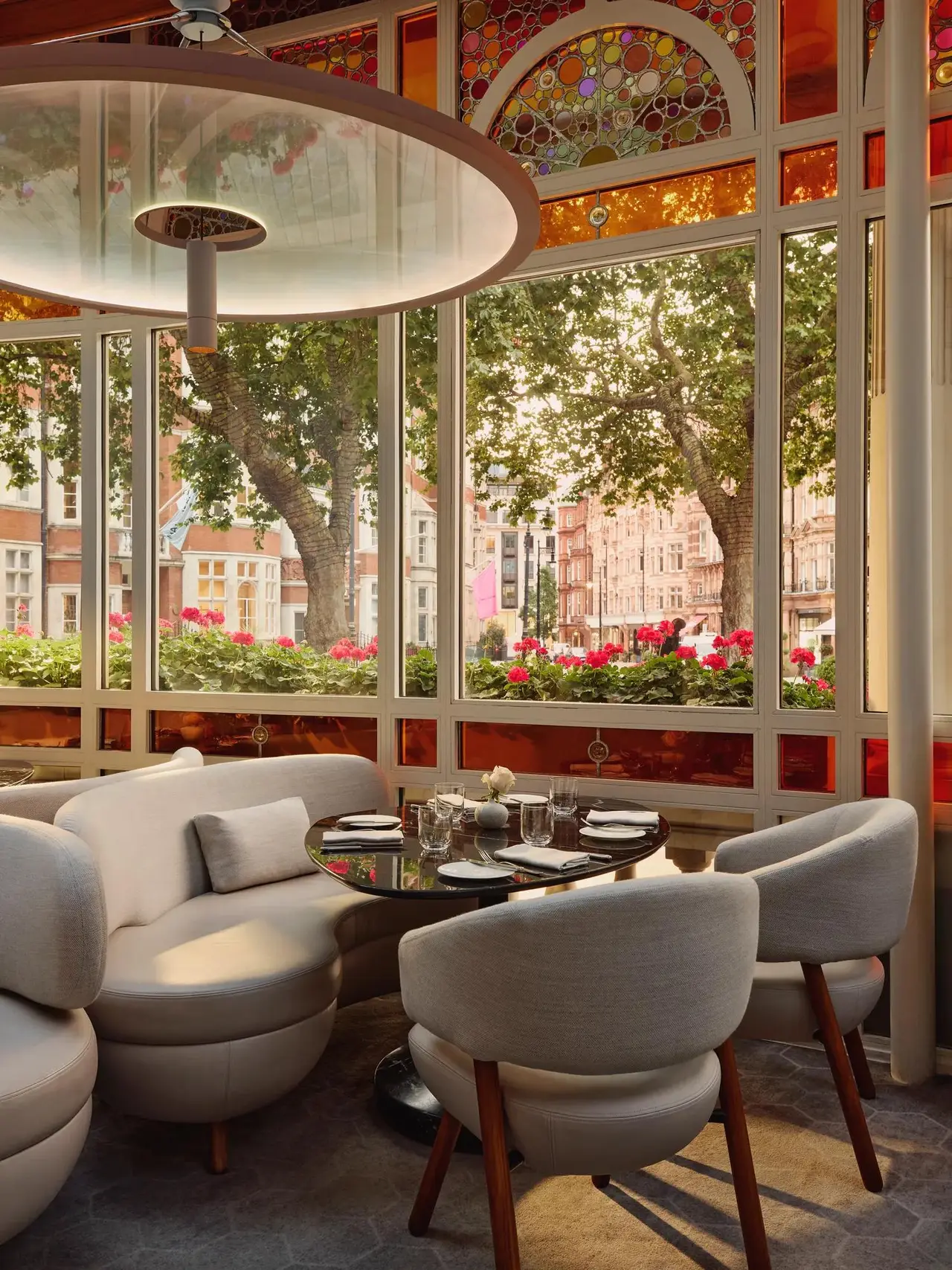 Jean-Georges: white tables in a glass veranda, stained glass, and trees and red brick beyond the panes