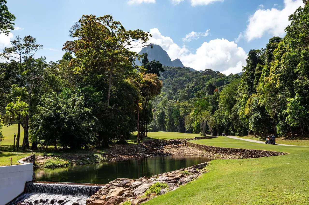 A hole of The Els Club Teluk Datai with a water hazard, forest and a granite peak behind