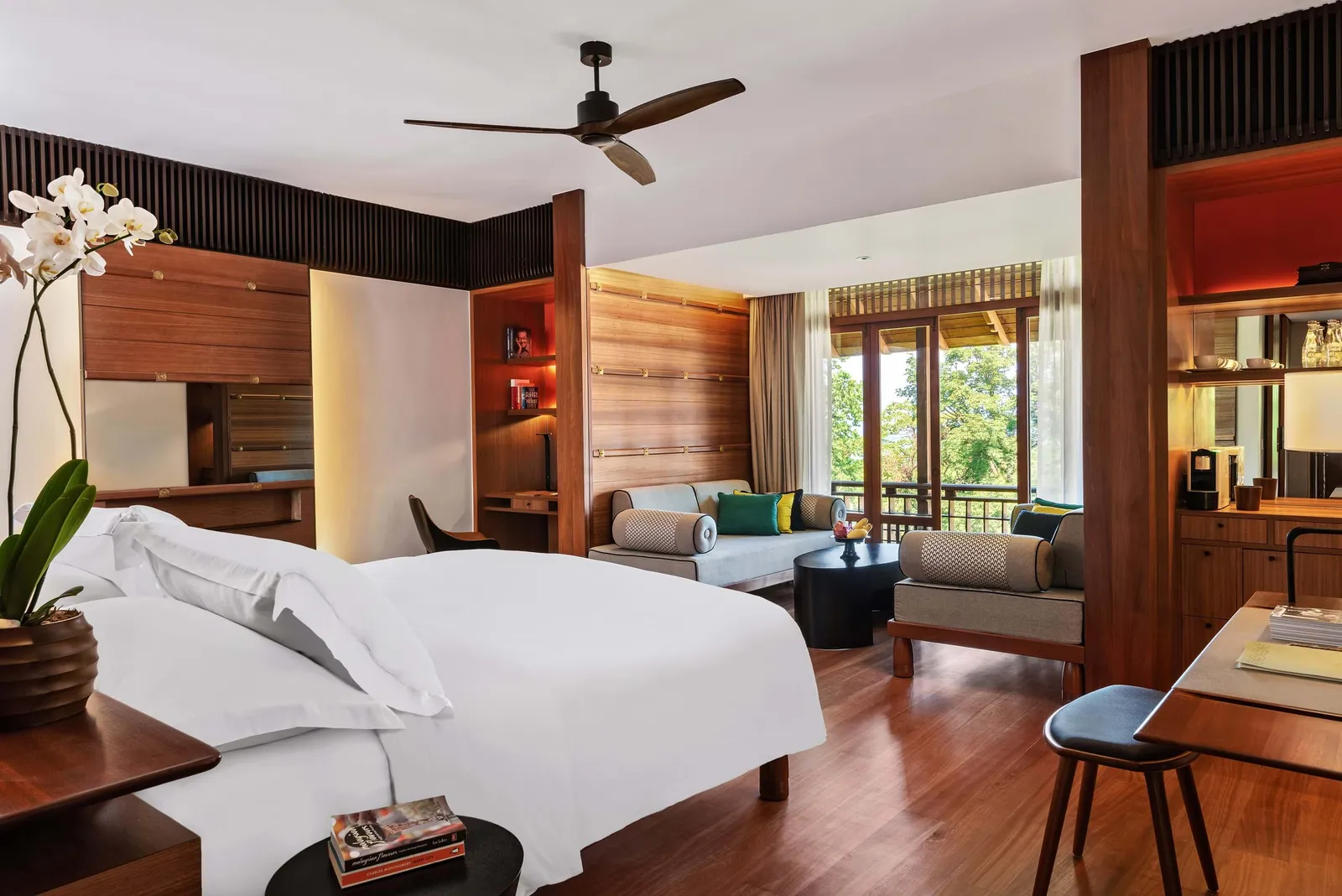 A Canopy Deluxe room: a white bed, timber panelling, a sofa at the window and trees outside