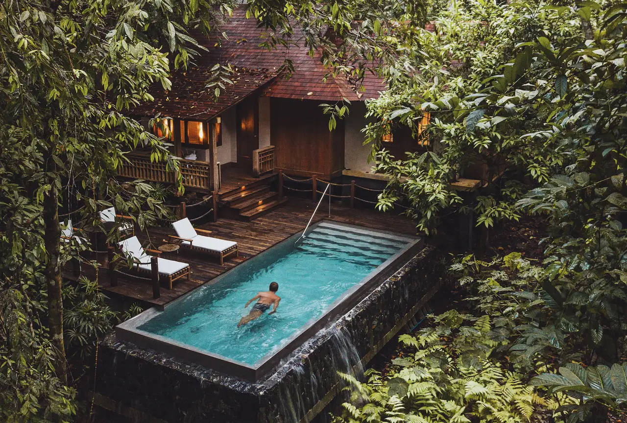 A guest swimming in a Rainforest Pool Villa’s private pool, the deck and villa among the trees