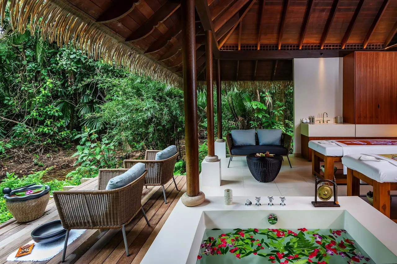 A spa villa open to the forest: treatment beds and a bath strewn with petals