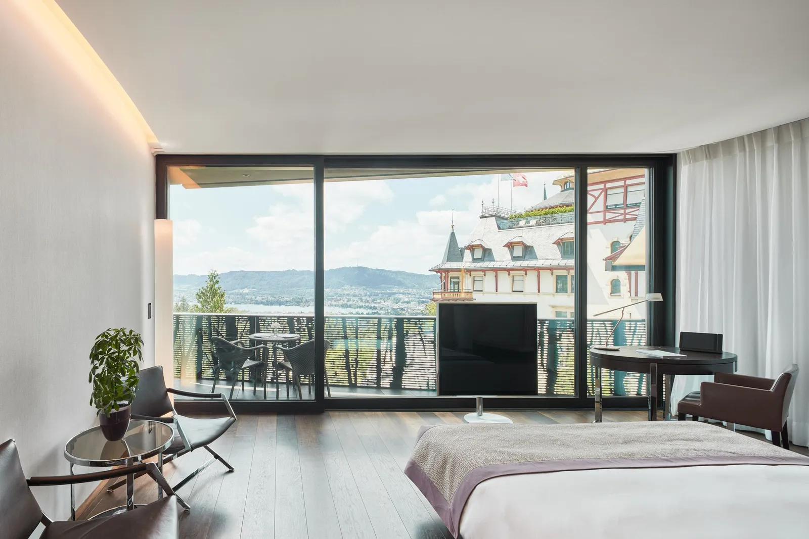 A Double Room Deluxe in the wing: the bed facing the balcony, with the towers of the historic building and Lake Zurich outside