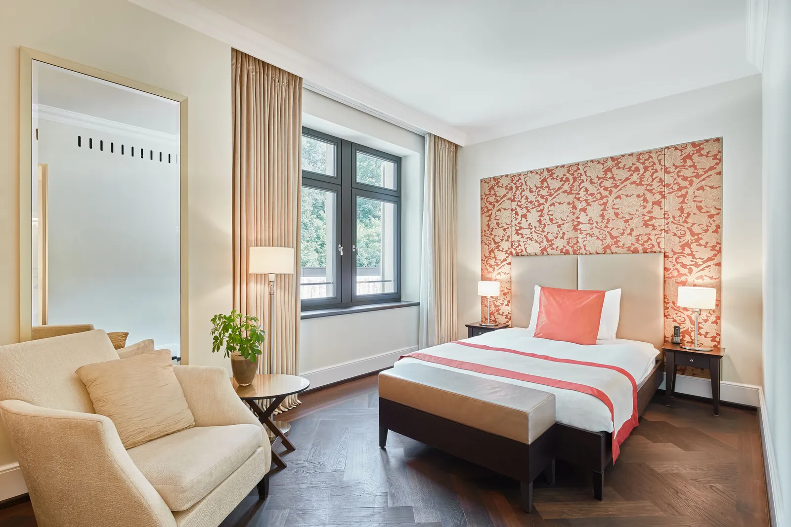 A Single Room Superior: the bed against a coral damask panel, an armchair and a window onto the trees