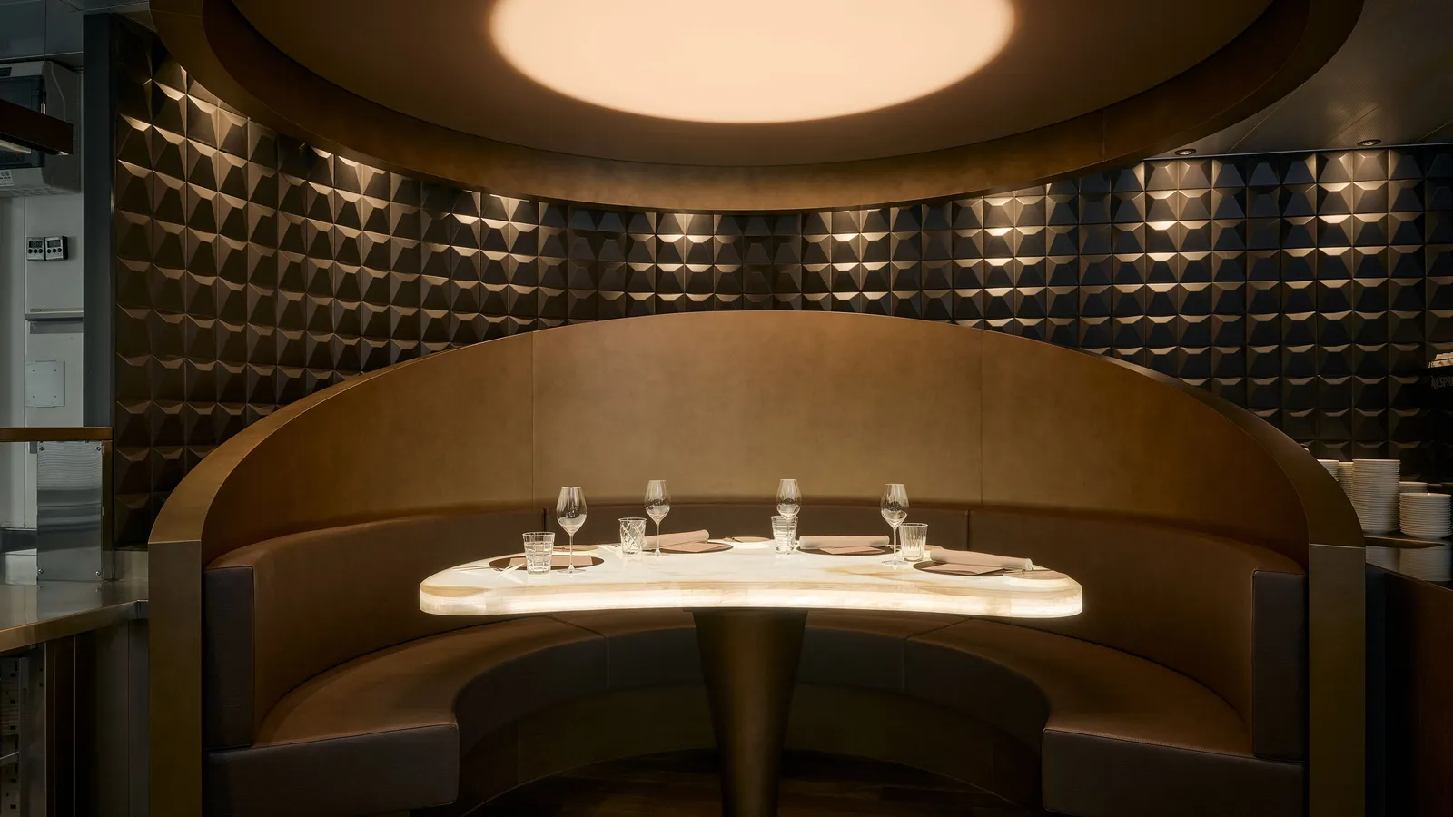 The Chef’s Table in the kitchen: a curved leather booth around a backlit onyx table laid for dinner
