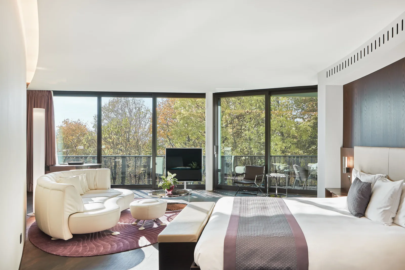 A Junior Suite Superior in the wing: the bed, a curved white sofa on a purple rug and windows onto the trees
