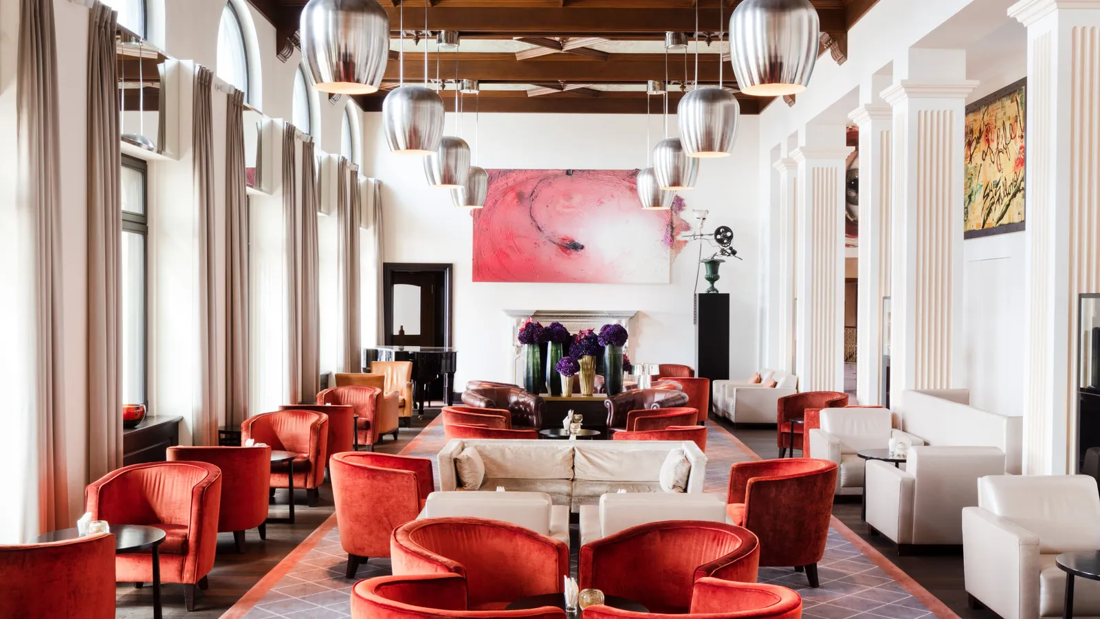 The lobby lounge: red velvet armchairs and white sofas under a painted coffered ceiling, a large pink painting above the fireplace