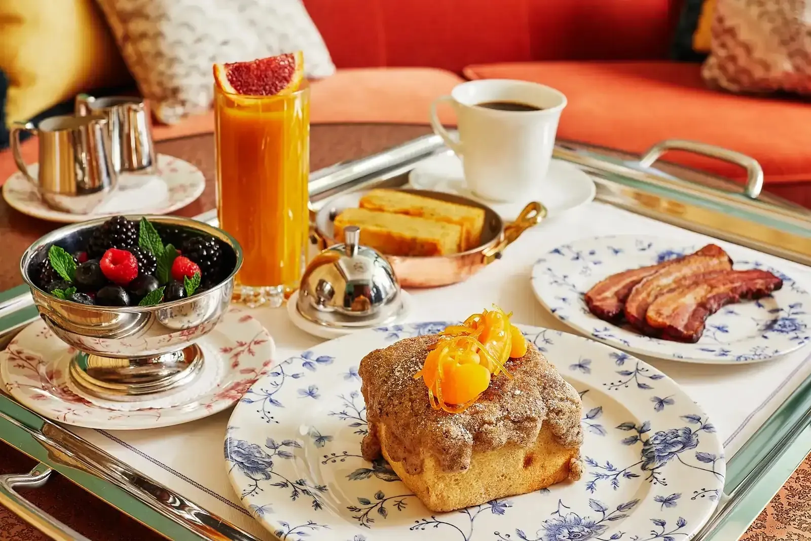 A breakfast tray: juice, coffee, berries, bacon and a pastry
