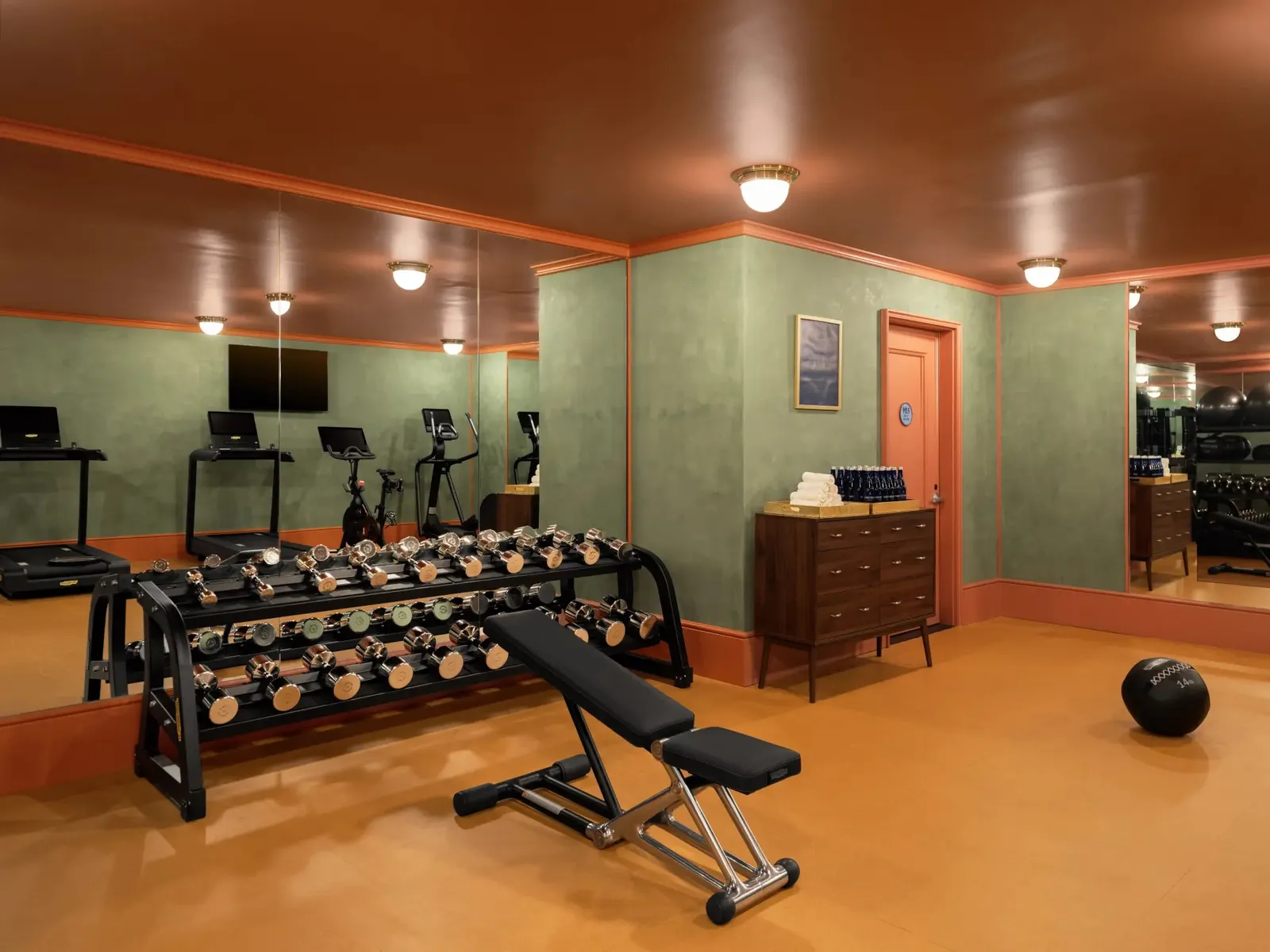 The gym with racks of dumbbells and treadmills under a copper ceiling