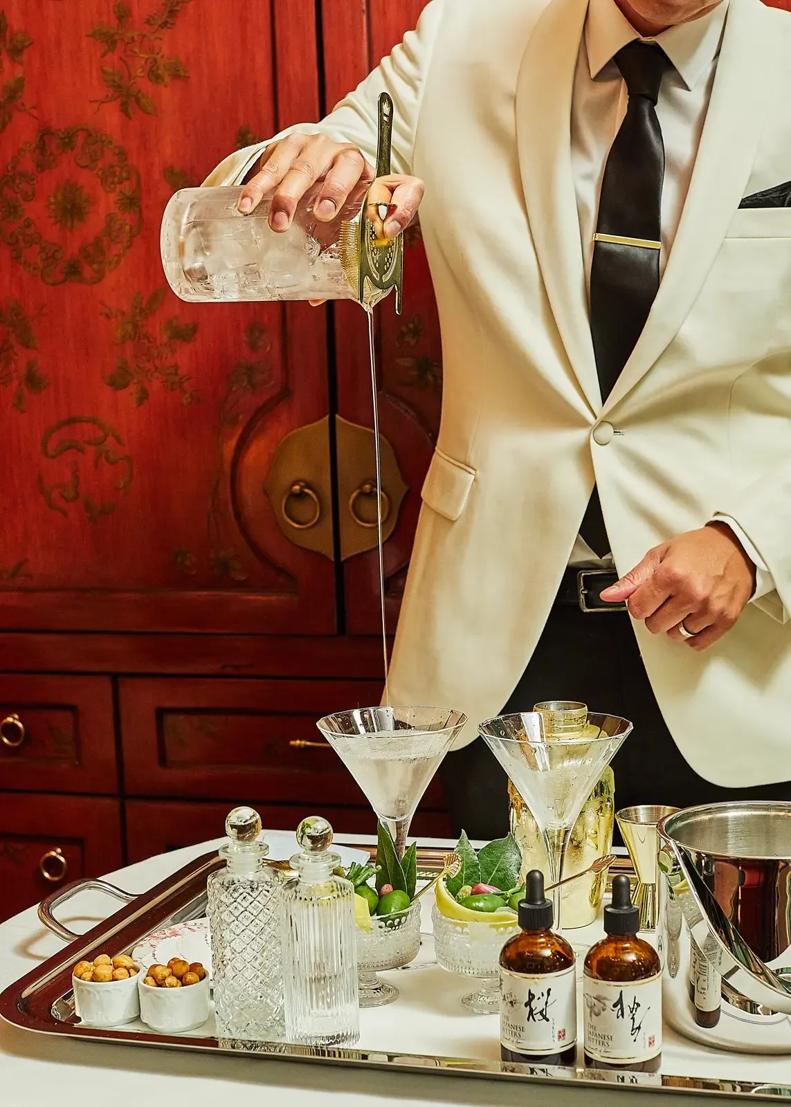 A butler in a white jacket pouring a martini from a silver cart