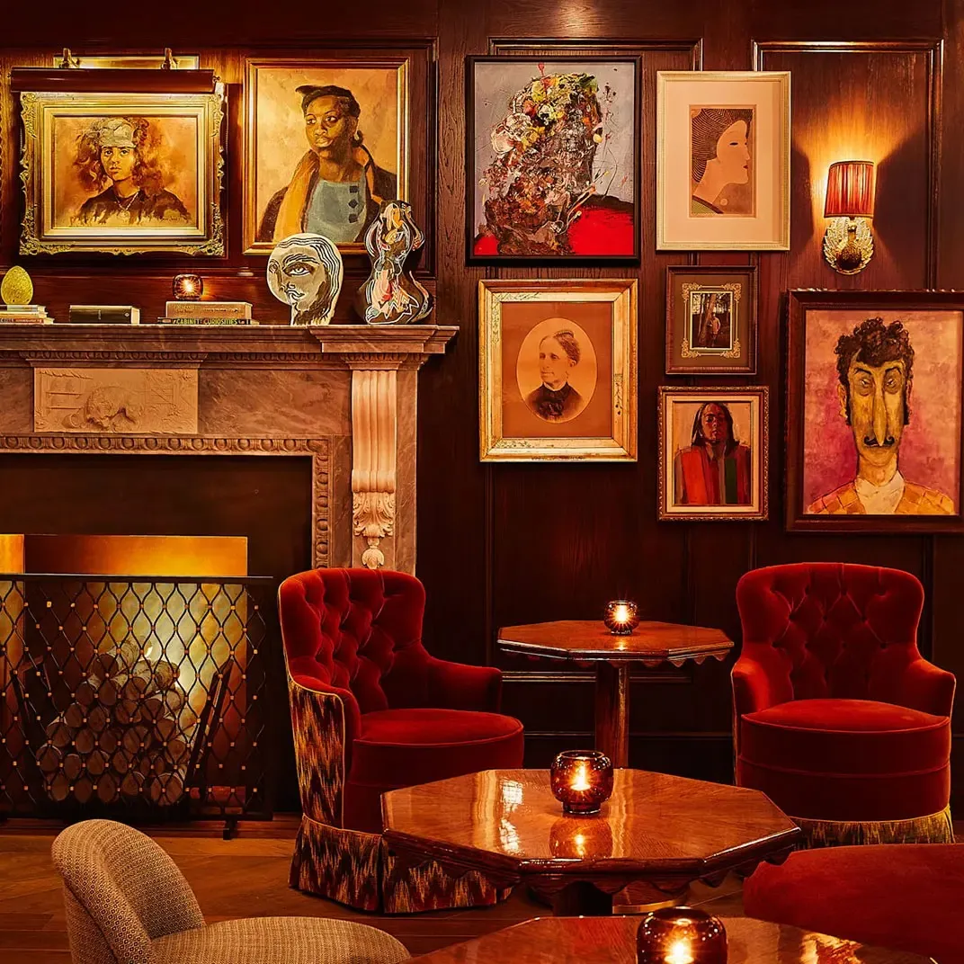 The Portrait Bar’s fireside corner, red velvet armchairs under the paintings