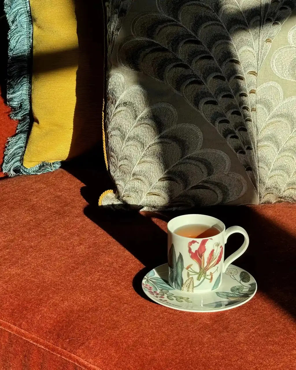A cup of tea on its saucer in the afternoon light, on a red carpet